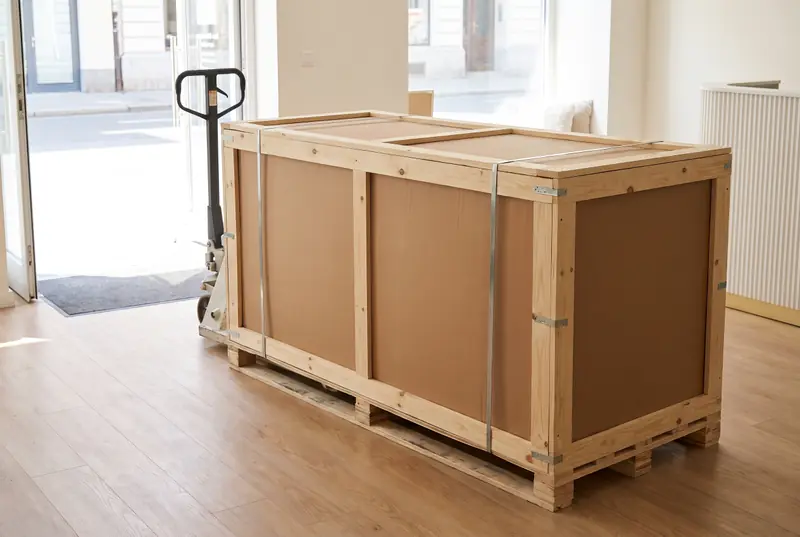 La table livrée sur palette, dans son carton cerclé d’un cadre en bois, à l’entrée d’un institut