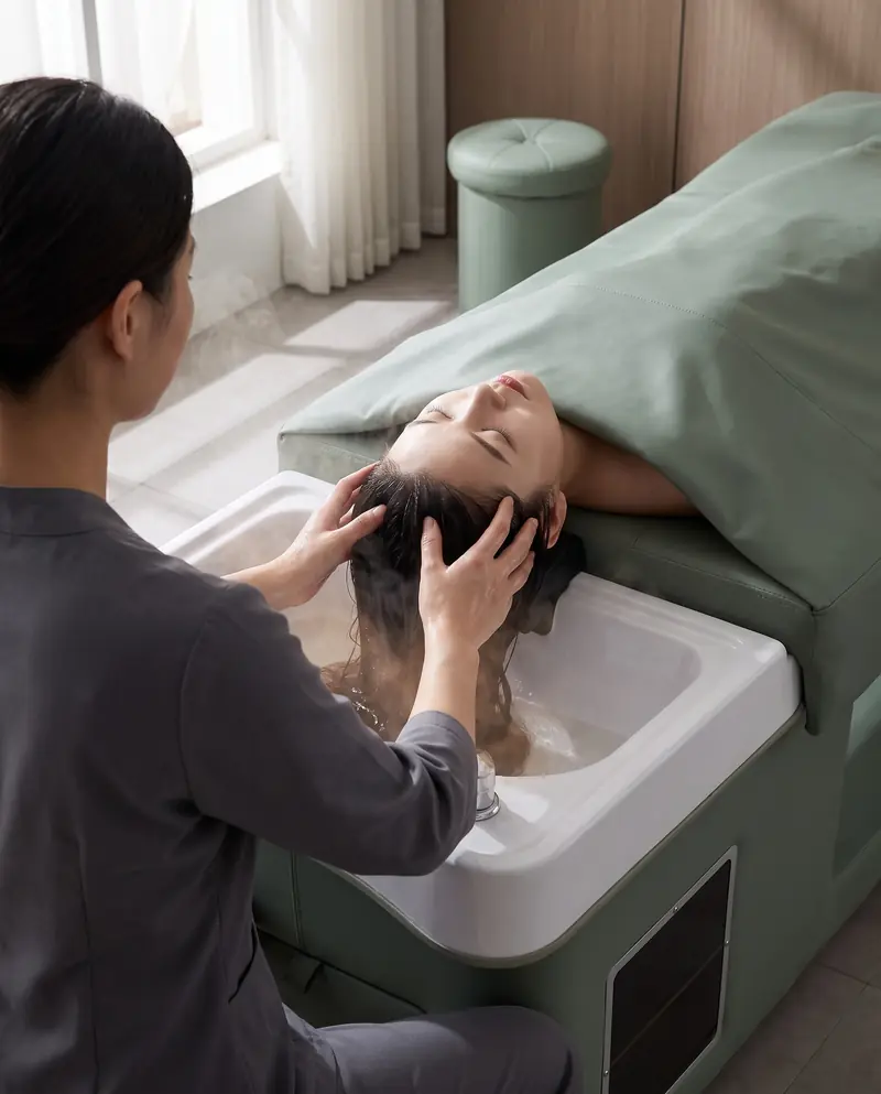Les mains de la praticienne massent le cuir chevelu de la cliente allongée, la nuque dans le bac